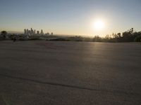 the sun sets over the city skyline in a beachfront area of a fenced off parking lot