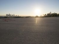 the sun sets over the city skyline in a beachfront area of a fenced off parking lot