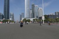 a city skyline with many tall buildings and people walking on a walkway along it, with a person in a stroller and one man walking away