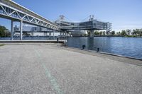 an empty road near the water near bridges and a pier on the river bank to the left side