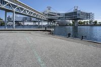 an empty road near the water near bridges and a pier on the river bank to the left side