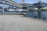 an empty road near the water near bridges and a pier on the river bank to the left side