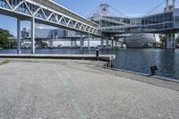 an empty road near the water near bridges and a pier on the river bank to the left side