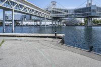 an empty road near the water near bridges and a pier on the river bank to the left side