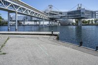 an empty road near the water near bridges and a pier on the river bank to the left side