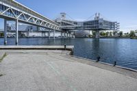 an empty road near the water near bridges and a pier on the river bank to the left side