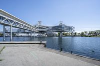 an empty road near the water near bridges and a pier on the river bank to the left side