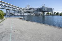 an empty road near the water near bridges and a pier on the river bank to the left side