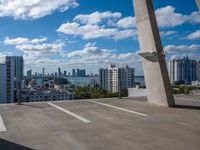 view from atop of a building with a parking area near by on the ground and large skyscrapers with high rise buildings in the distance