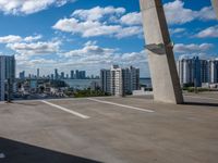 view from atop of a building with a parking area near by on the ground and large skyscrapers with high rise buildings in the distance