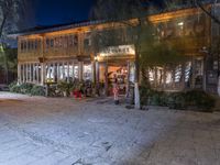 people are walking and walking down the street at night time at a city square, surrounded by trees