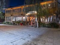 people are walking and walking down the street at night time at a city square, surrounded by trees