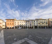 an empty square has people walking in it with a clock tower and arched archways