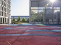 a large red basketball court with graffiti all over it with the sun in front of tall buildings