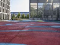 a large red basketball court with graffiti all over it with the sun in front of tall buildings