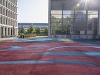 a large red basketball court with graffiti all over it with the sun in front of tall buildings