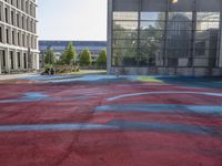 a large red basketball court with graffiti all over it with the sun in front of tall buildings