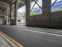 a person on a bicycle riding along a city sidewalk next to an overpass and another building