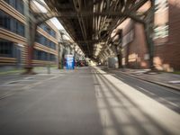 an empty city street lined with tall buildings and steel bridges, with the shadows coming on the pavement, and the tops of a bridge above them