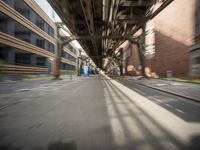 an empty city street lined with tall buildings and steel bridges, with the shadows coming on the pavement, and the tops of a bridge above them