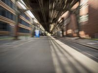 an empty city street lined with tall buildings and steel bridges, with the shadows coming on the pavement, and the tops of a bridge above them