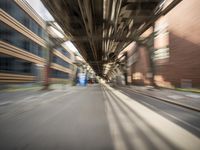 an empty city street lined with tall buildings and steel bridges, with the shadows coming on the pavement, and the tops of a bridge above them