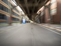 an empty city street lined with tall buildings and steel bridges, with the shadows coming on the pavement, and the tops of a bridge above them