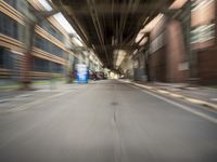 an empty city street lined with tall buildings and steel bridges, with the shadows coming on the pavement, and the tops of a bridge above them