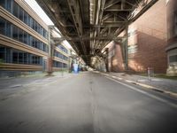 an empty city street lined with tall buildings and steel bridges, with the shadows coming on the pavement, and the tops of a bridge above them