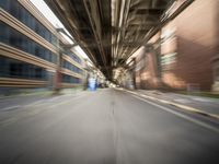 an empty city street lined with tall buildings and steel bridges, with the shadows coming on the pavement, and the tops of a bridge above them