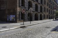 a street corner with a bricked curb, and cobblestone walkway with parking spaces on either side of it