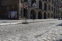 a street corner with a bricked curb, and cobblestone walkway with parking spaces on either side of it