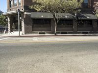 the fire hydrant is next to the street on the corner of the street that is painted black and has an awning