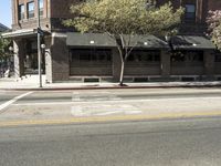 the fire hydrant is next to the street on the corner of the street that is painted black and has an awning