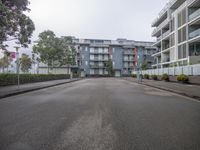 a view from the sidewalk of a city street in front of buildings with trees and shrubs lining both sides