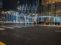 city street with empty traffic and glass building in background at night, near sidewalk and bench