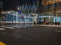 city street with empty traffic and glass building in background at night, near sidewalk and bench