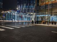 city street with empty traffic and glass building in background at night, near sidewalk and bench