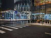 city street with empty traffic and glass building in background at night, near sidewalk and bench