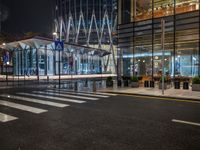 city street with empty traffic and glass building in background at night, near sidewalk and bench