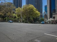 a car on a city street with high rise buildings in the background, surrounded by trees