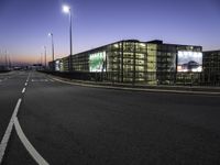 a highway going into a parking lot with cars and a building in the background at dusk