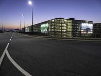 a highway going into a parking lot with cars and a building in the background at dusk