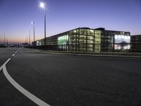 a highway going into a parking lot with cars and a building in the background at dusk