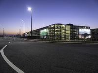 a highway going into a parking lot with cars and a building in the background at dusk