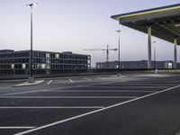 an empty car park with street lights on a blue dusk evening, with a parking lot in the foreground