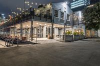 a restaurant with lights and outdoor seating on the street at night time on an urban street