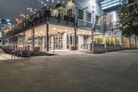 a restaurant with lights and outdoor seating on the street at night time on an urban street