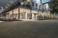 a restaurant with lights and outdoor seating on the street at night time on an urban street