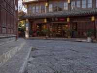 a street outside a large stone building with wooden doors and windows decorated with asian lanterns